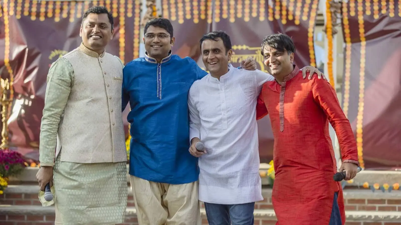 Four men in colourful kurtas stand together at the Diwali celebration