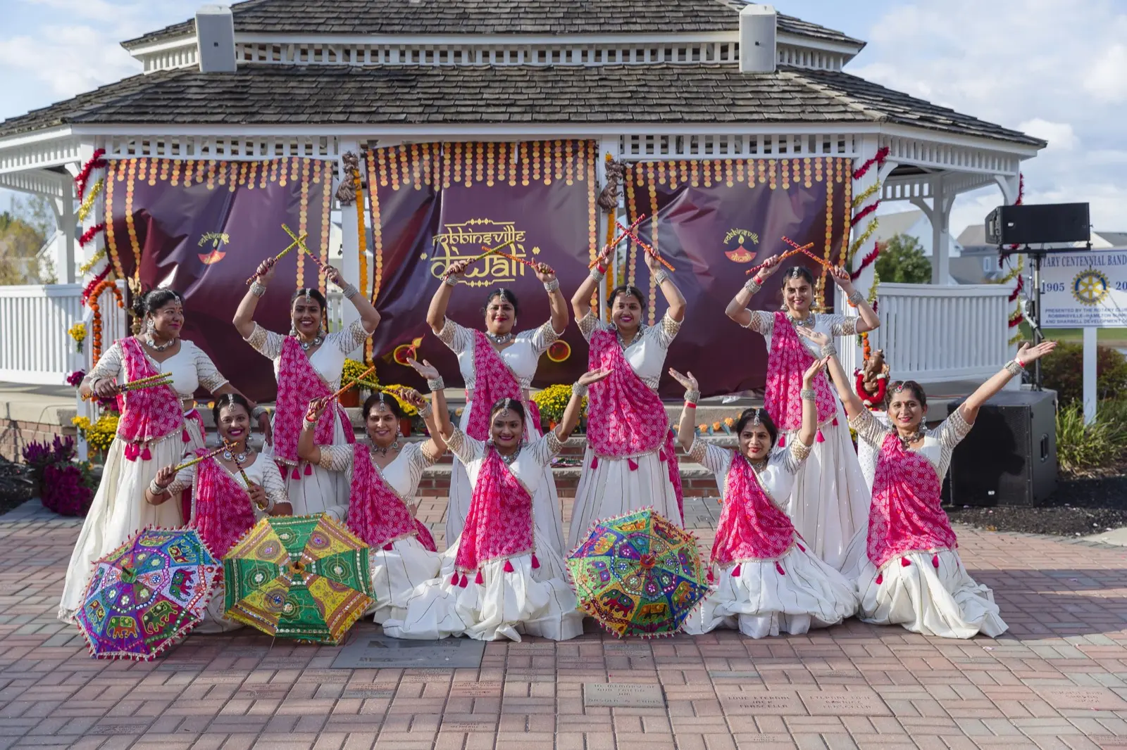 Dancers in white and pink with embroidered umbrellas perform in front of the Robbinsville gazebo