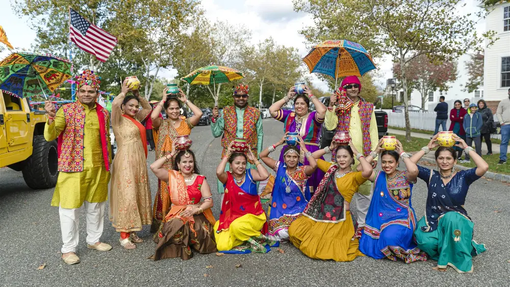 A folk troupe with embroidered umbrellas and an American flag poses during the Diwali Parade