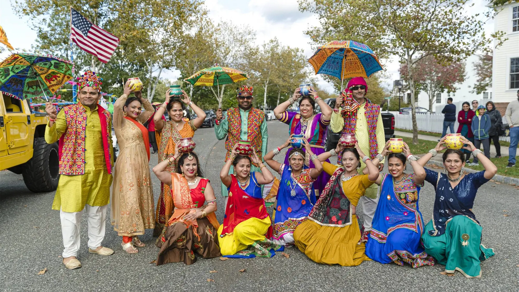 A folk troupe with embroidered umbrellas and an American flag poses during the Diwali Parade
