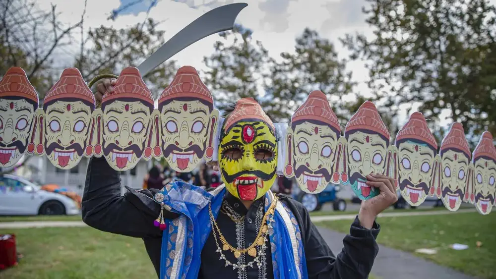A performer in a painted Ravan mask stands before a row of ten-headed effigy masks at Diwali