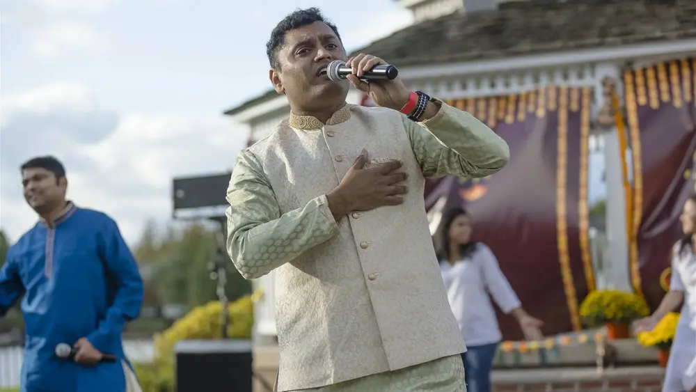 A singer in a cream kurta performs into a microphone at the Robbinsville Diwali celebration