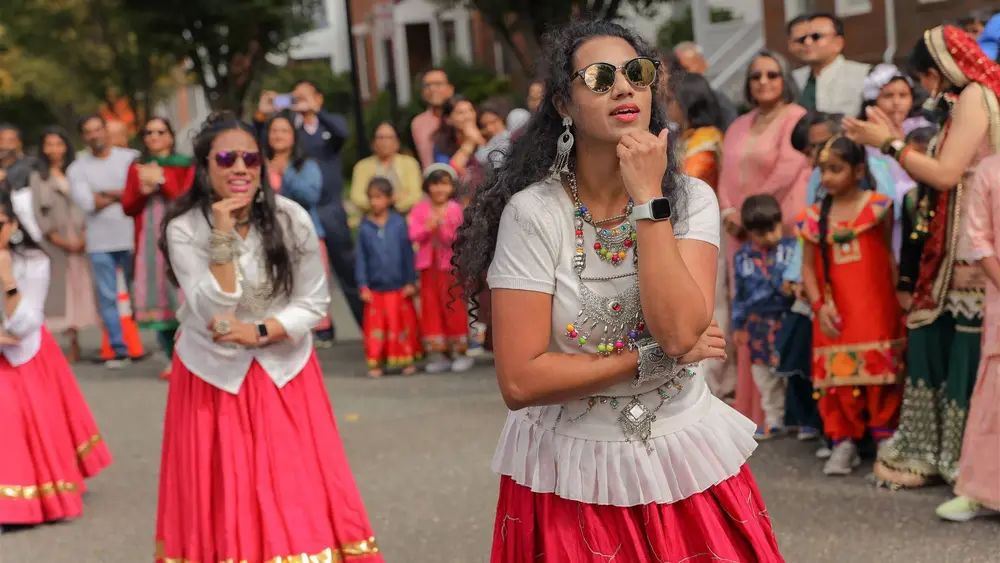 Women in red and gold dance and clap along the Diwali Parade route