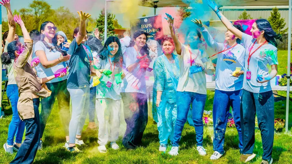 Friends throw colour powder into the air at Robbinsville Holi