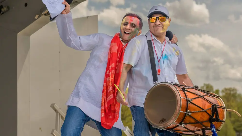 A dhol drummer and a friend in Holi colour celebrate with arms raised