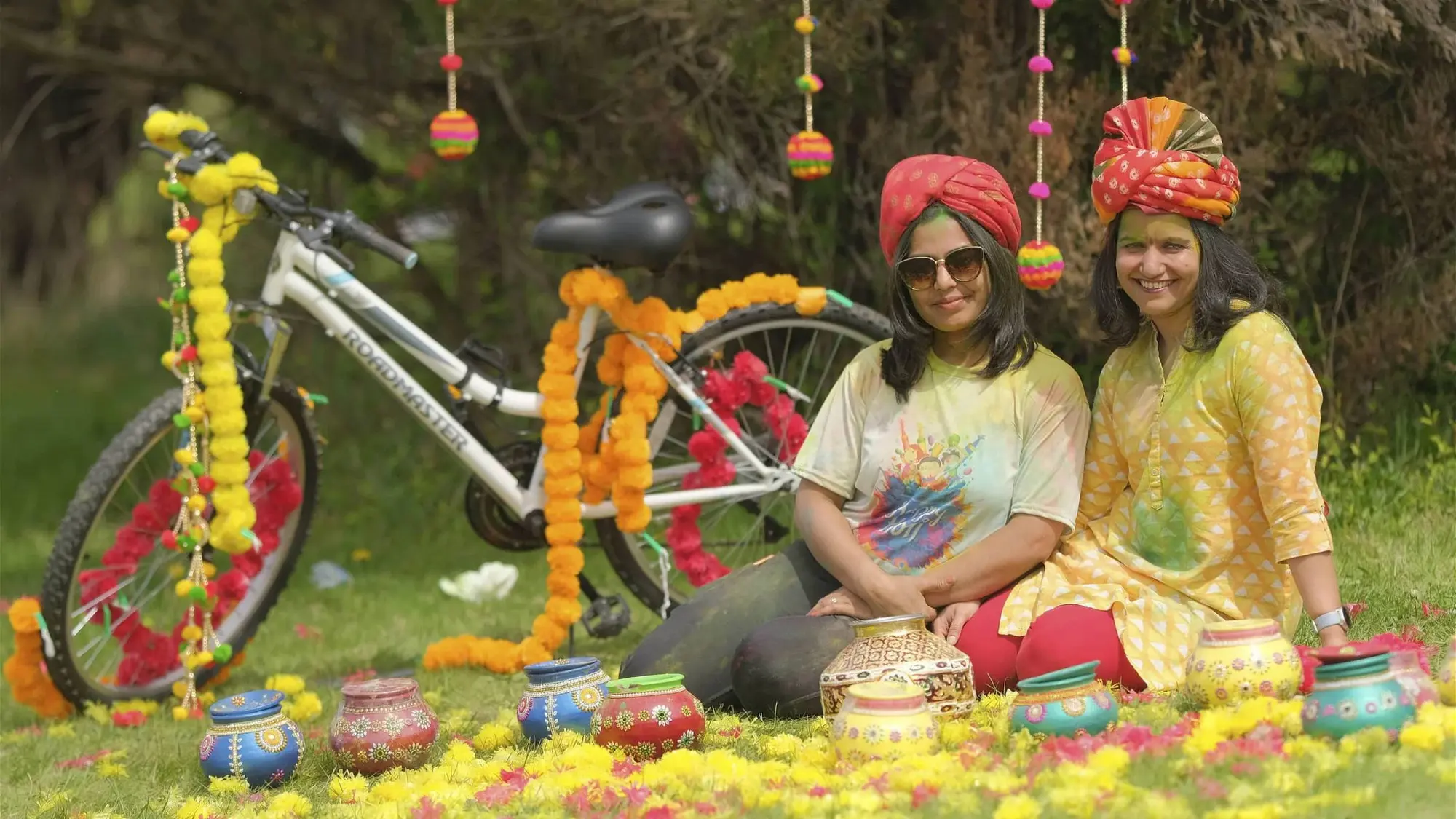 Women pose beside a bicycle decorated with marigolds at Vasant Utsav