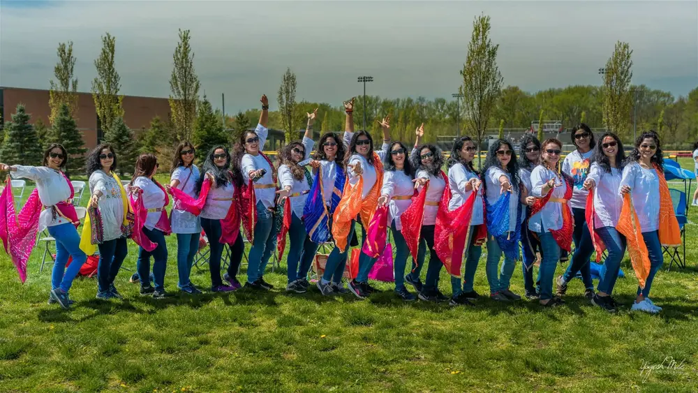 A long line of dancers waves orange and pink dupattas across the field