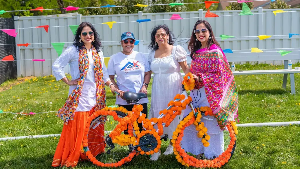 Friends in Holi colour stand beside a marigold-covered bicycle