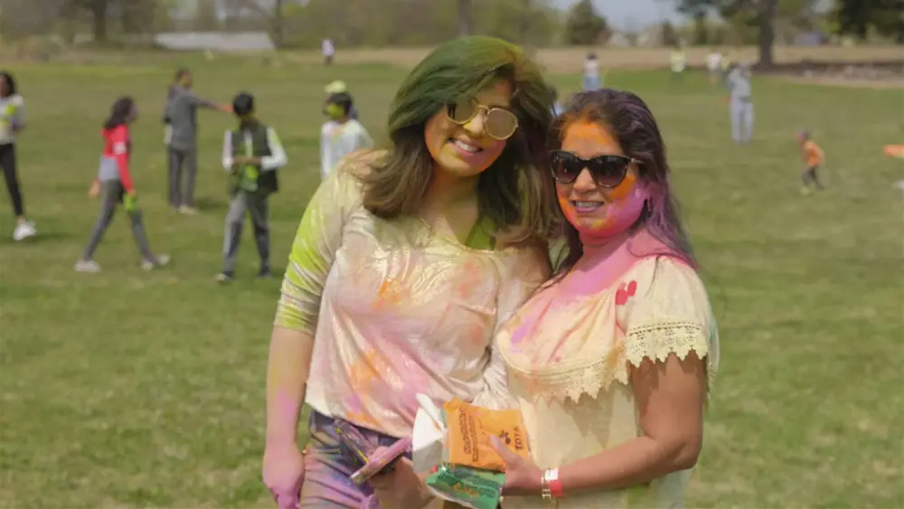 Two women in Holi colour share a moment on the grass at Vasant Utsav