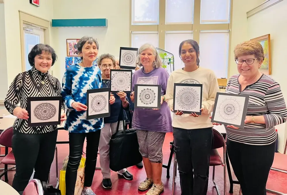 Youth volunteers and seniors hold up the framed mandala artwork they made together
