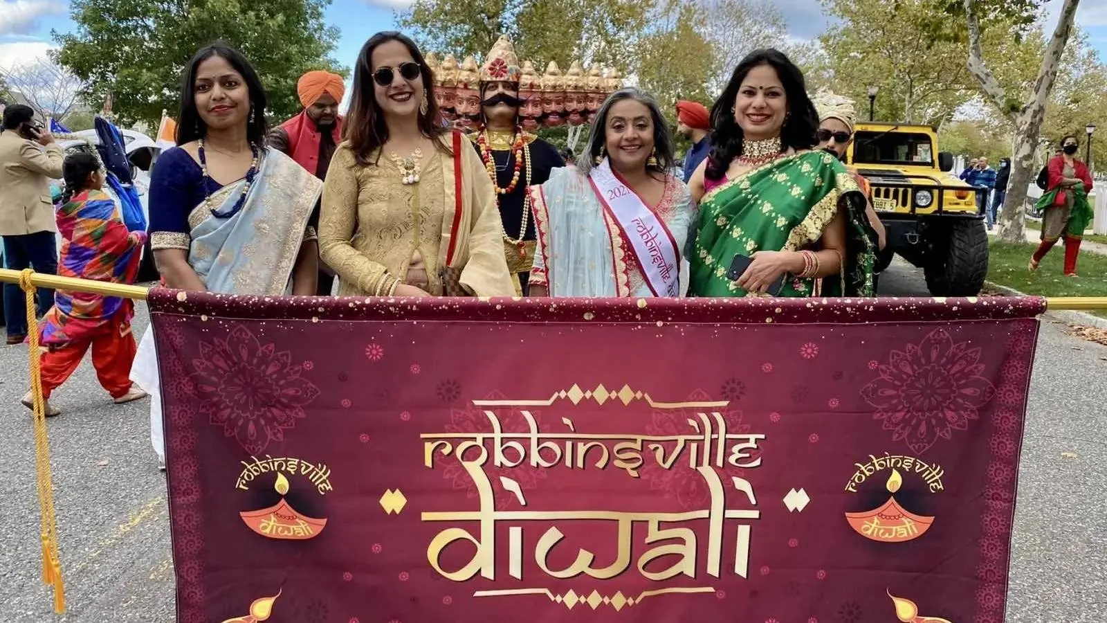 Women carry the maroon and gold Robbinsville Diwali banner at the head of a parade group