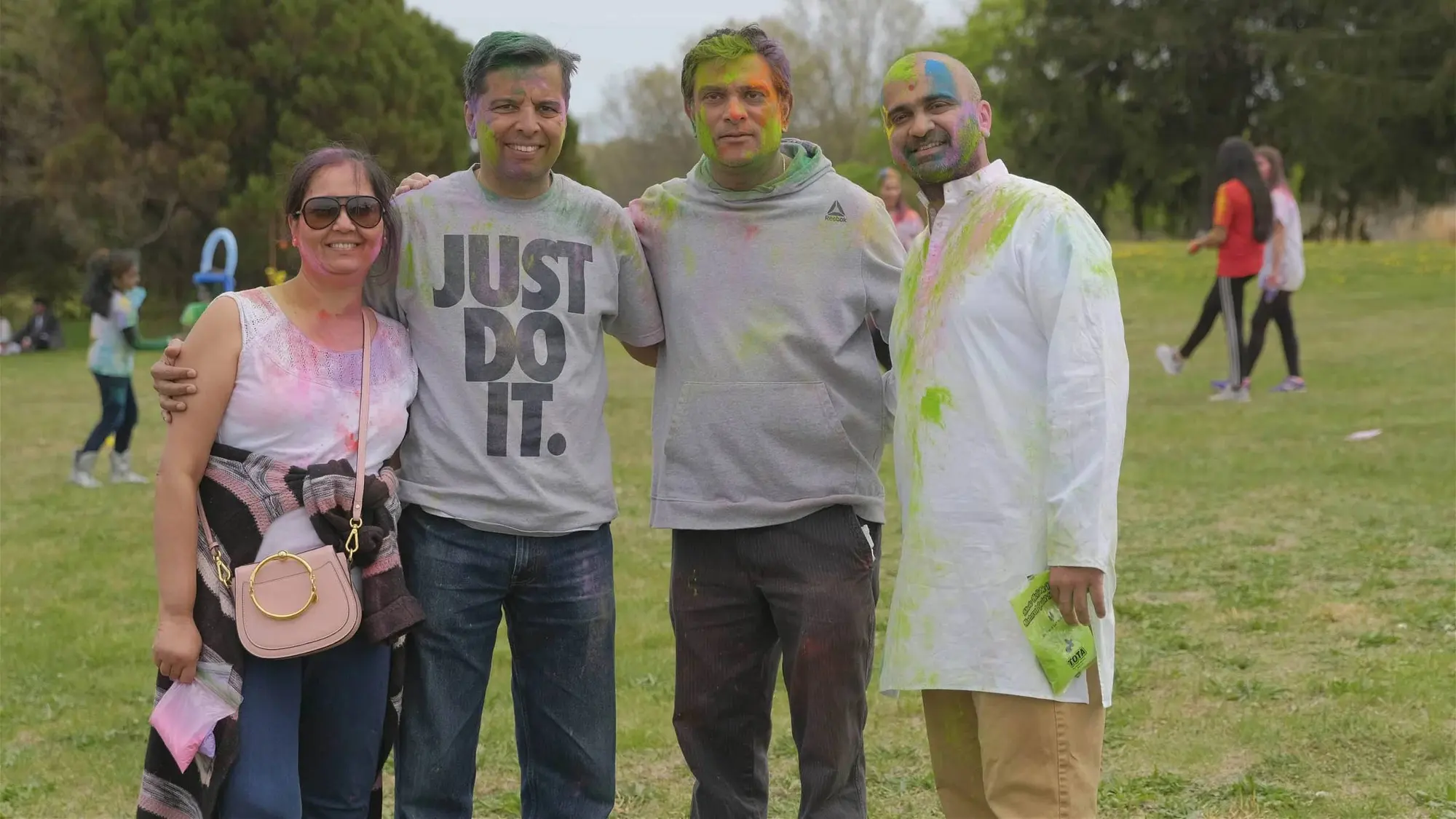 Friends covered in Holi colour laugh together on the field at Robbinsville Holi