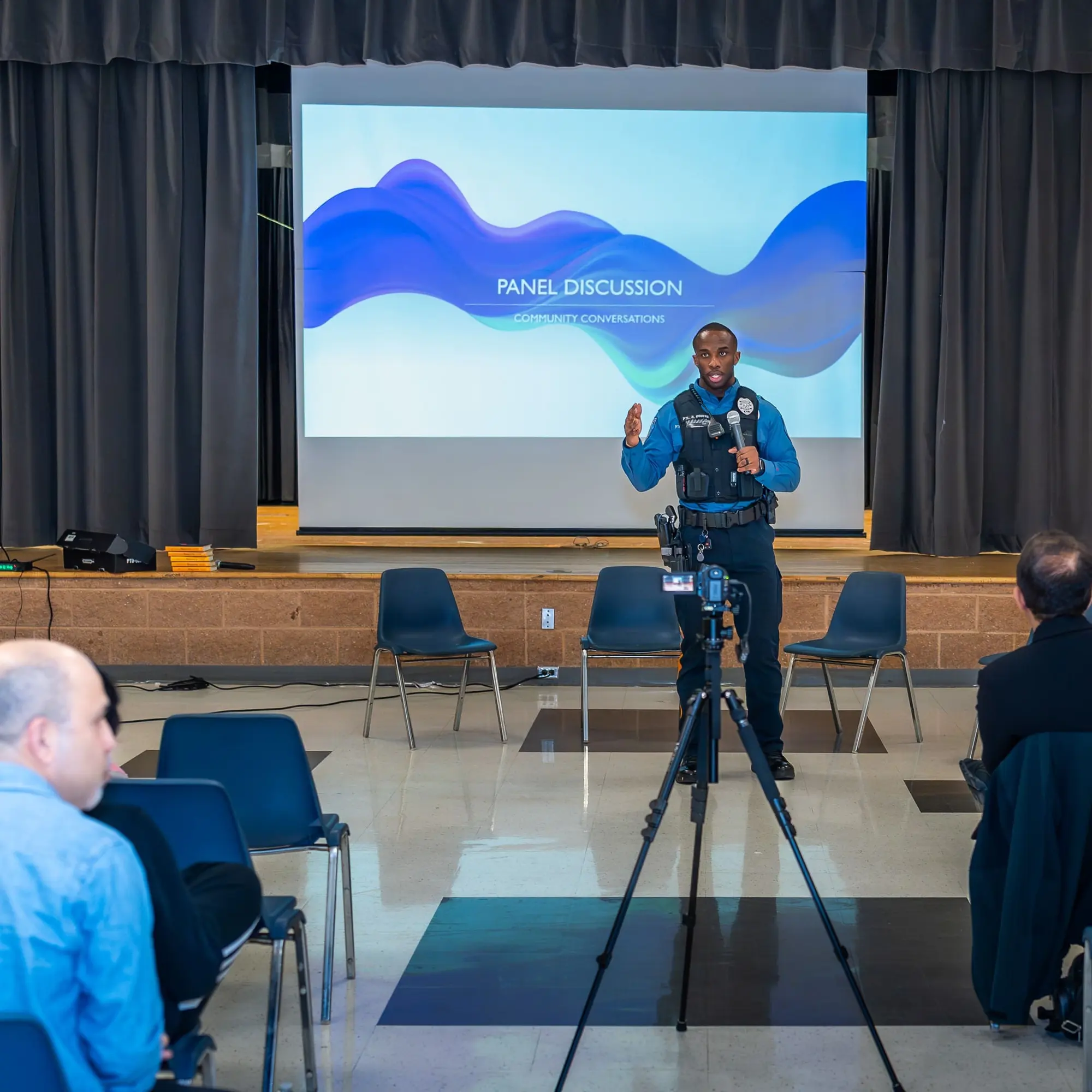 A moderator stands at the front of the room during Sangat