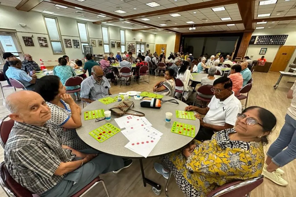 Seniors play bingo around a round table at a Sanskriti afternoon