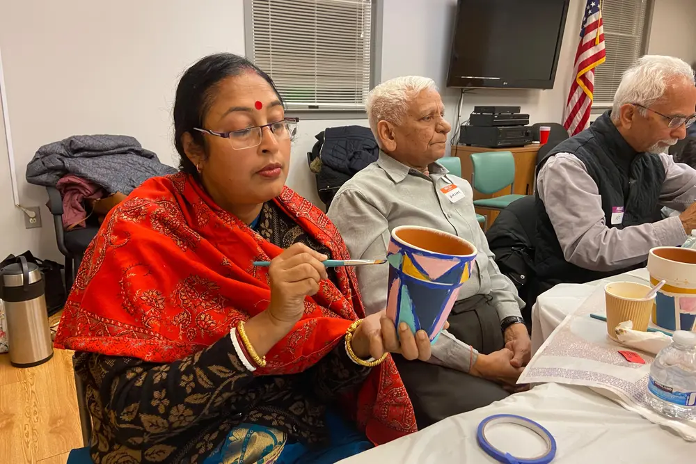 A Sanskriti member in a red shawl paints a clay pot at a senior craft afternoon