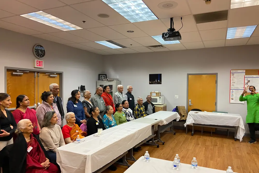 A full room of seniors at long tables during a Sanskriti senior social