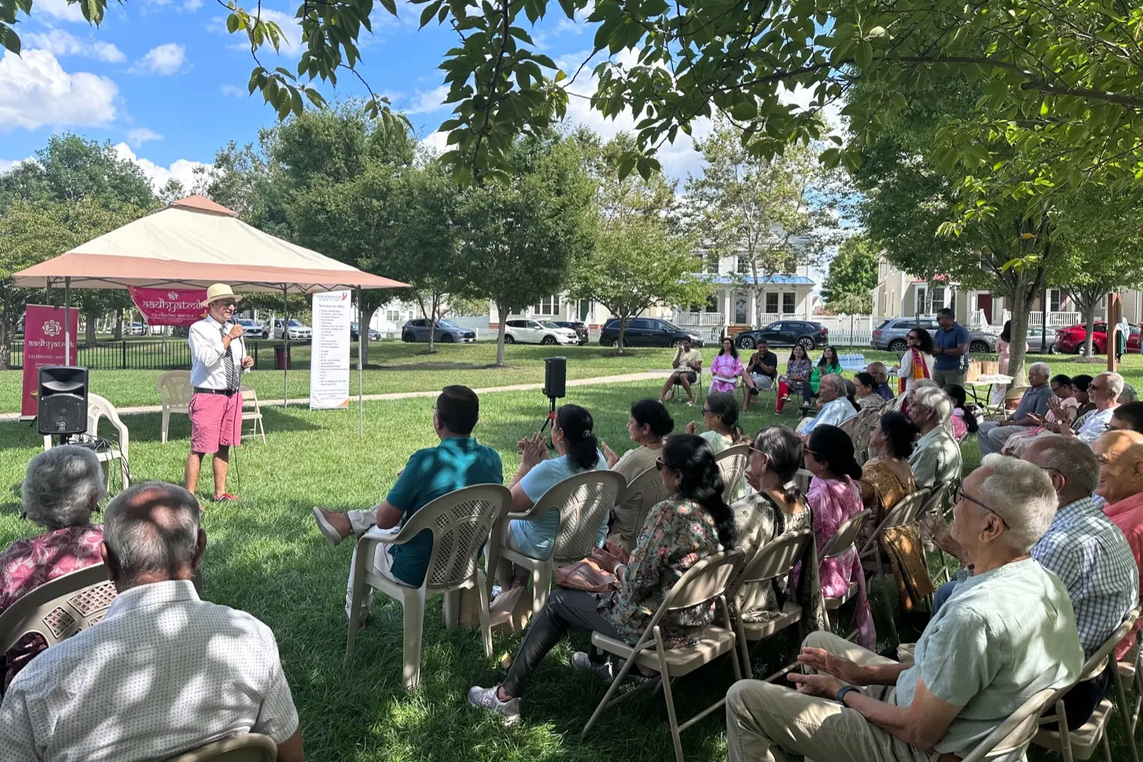 Seniors gathered on folding chairs under shade trees at a Sanskriti outdoor social
